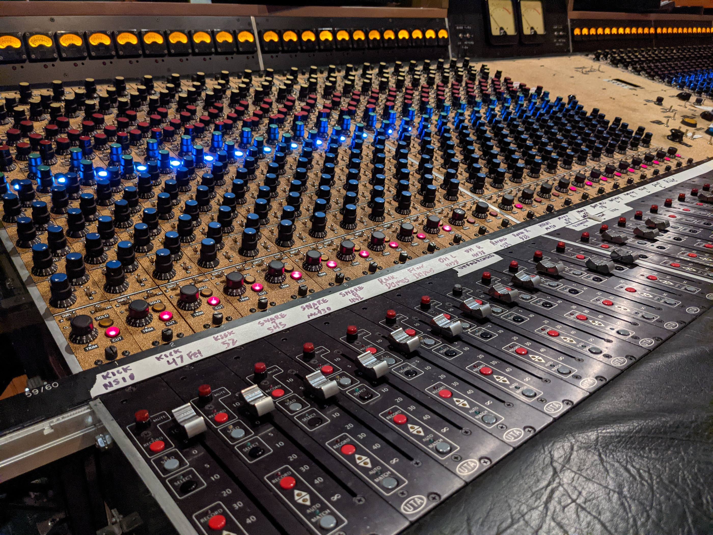 A recording console lit by rows of illuminated knobs.